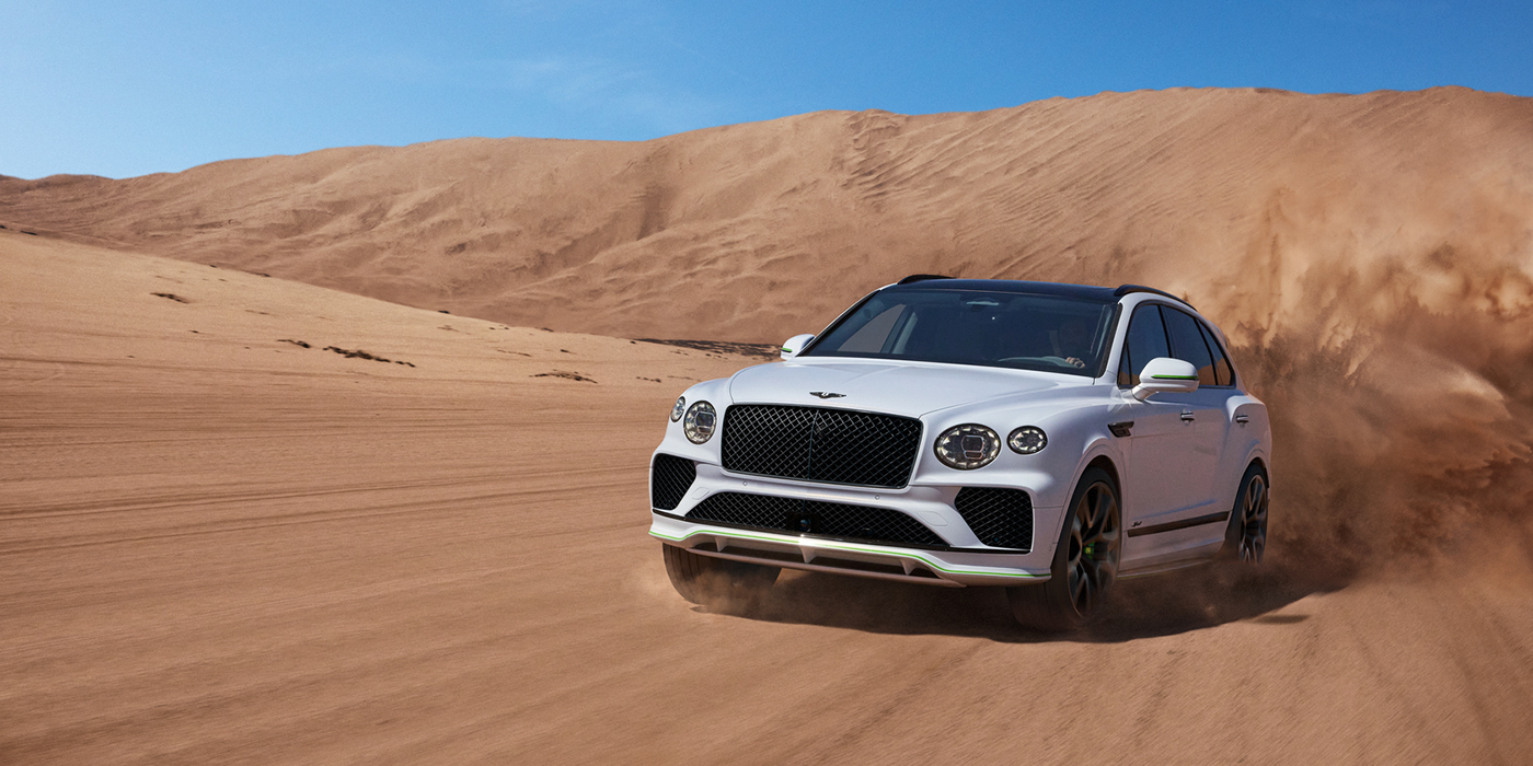 Bentley Riyadh Bentley Bentayga Speed SUV front three quarter in Snow Quarts Pearlescent by Mulliner white paint driving dynamically through the desert