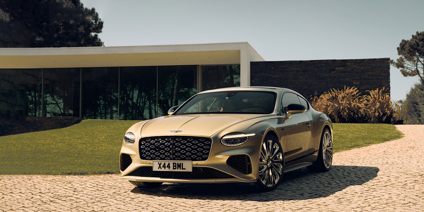 Bentley Riyadh Bentley Continental GT Mulliner coupe front three quarters in Patina paint parked outside a glass fronted building with a grass lawn behind it
