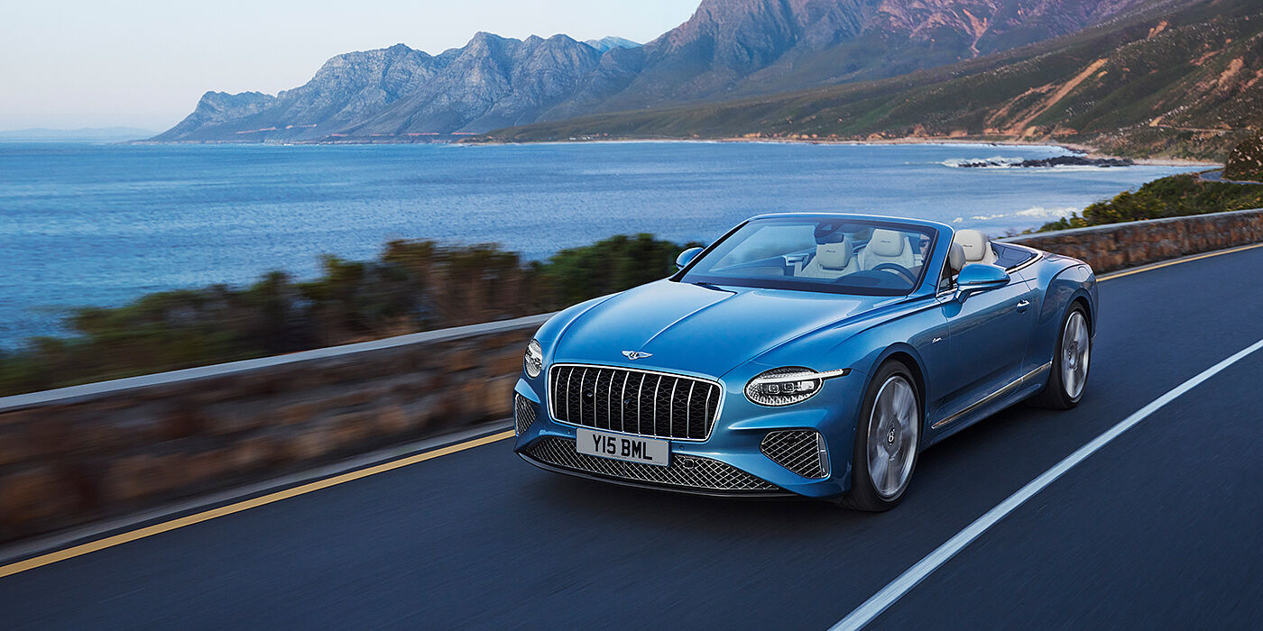 Bentley Riyadh New Bentley Continental GTC Azure convertible in Light Windsor blue paint with 22 inch Azure wheels and chrome grill, driving dynamically by the sea