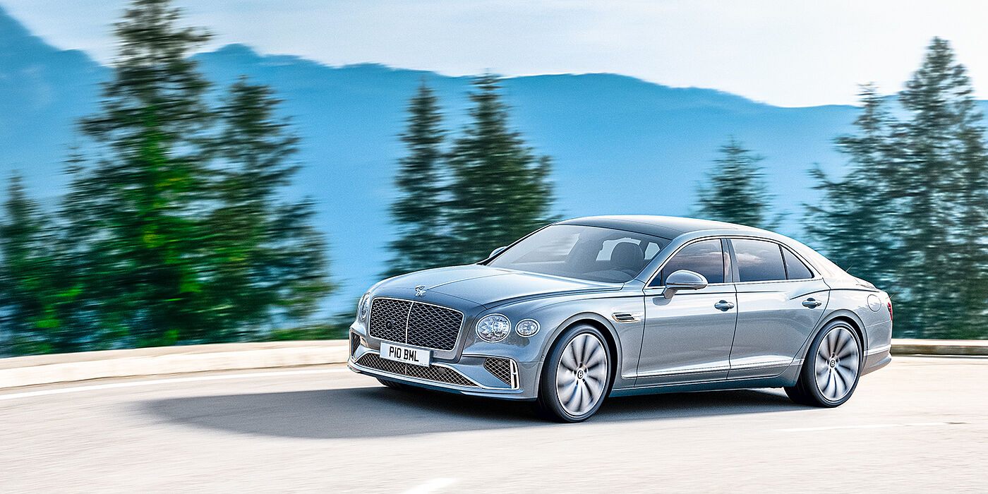 Bentley Riyadh New Bentley Flying Spur sedan side view in Silverlake paint with ten spoke wheels and chrome matrix grille driving dynamically on a mountain road