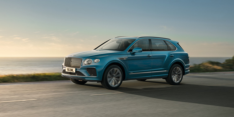 Bentley Riyadh Bentley Bentayga Azure SUV in Topaz blue paint driving dynamically by the ocean with 22 inch 10 spoke directional wheels