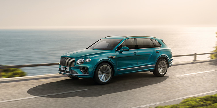 Bentley Riyadh Bentley Bentayga Extended Wheelbase Azure SUV in Topaz blue paint driving dynamically by the ocean