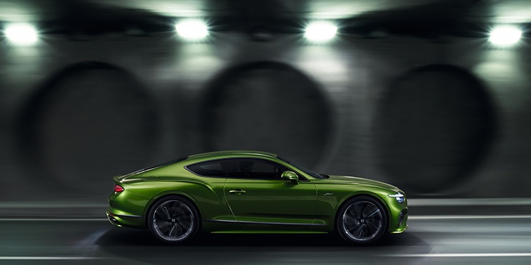 Bentley Riyadh Bentley Continental GT Speed coupe profile in Tourmaline Green driving dynamically past a concrete wall at night