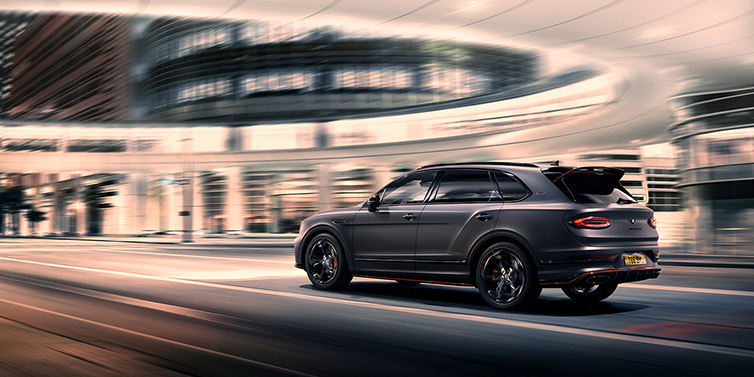 Bentley Riyadh Bentley Bentayga S Black Edition SUV rear three quarter in Anthracite Satin paint driving dynamically through a city at night