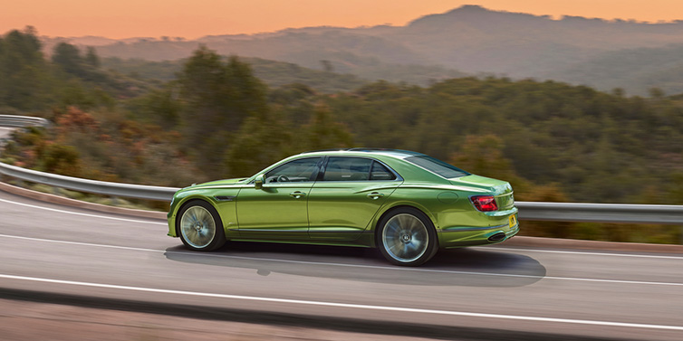 Bentley Riyadh Bentley Flying Spur Speed sedan side profile in Tourmaline Green paint driving dynamically on a mountain road at sunset