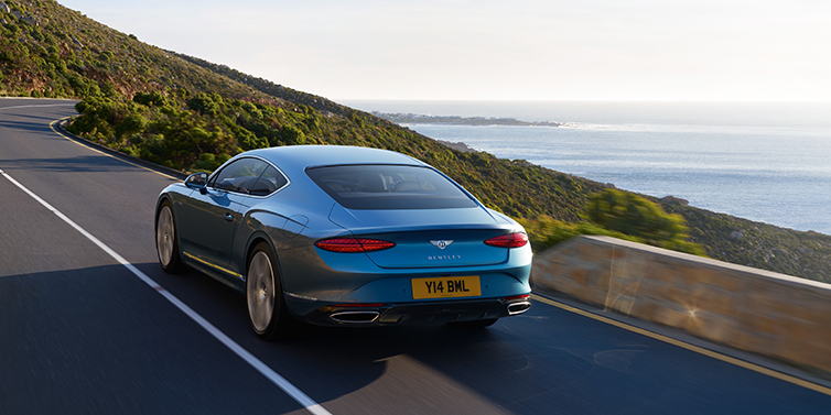 Bentley Riyadh New Bentley Continental GT Azure coupe in Light Windsor blue paint seen from the rear driving dynamically on a seaside road