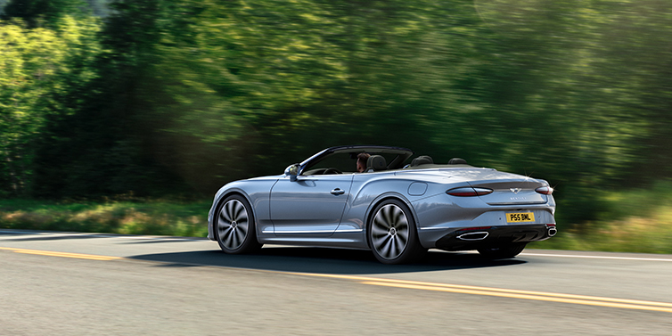 Bentley Riyadh New Bentley Continental GTC convertible side view in Silverlake paint with 22 inch ten spoke wheels driving dynamically on a country road