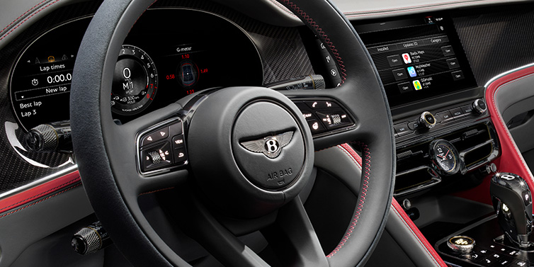 Bentley Riyadh Bentley Flying Spur Speed sedan front interior detail showing steering wheel and driver screens surrounded with Hotspur red and Gravity Grey hides